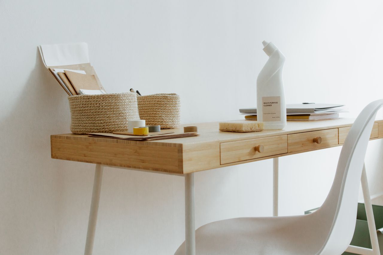 A tidy and well-arranged home office workspace featuring cleaning supplies, documents, and storage containers.